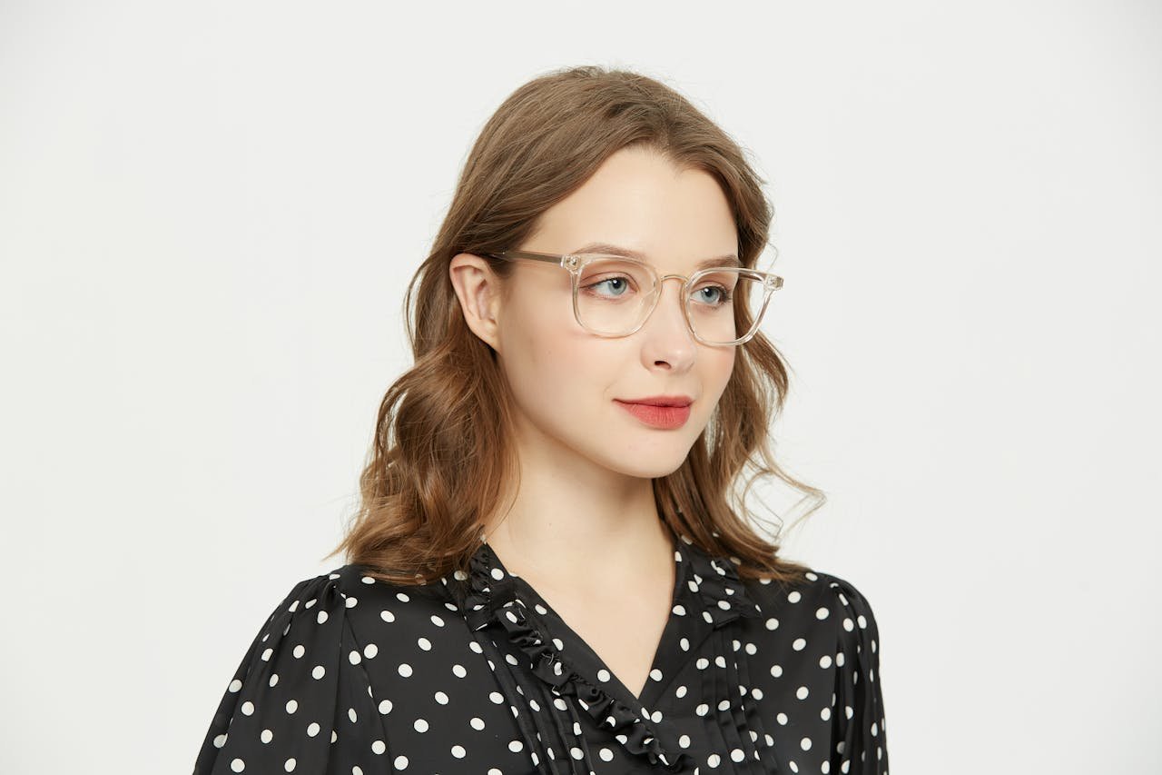 Home Elegant portrait of a young woman in polka dot shirt and eyeglasses, showcasing contemporary fashion.