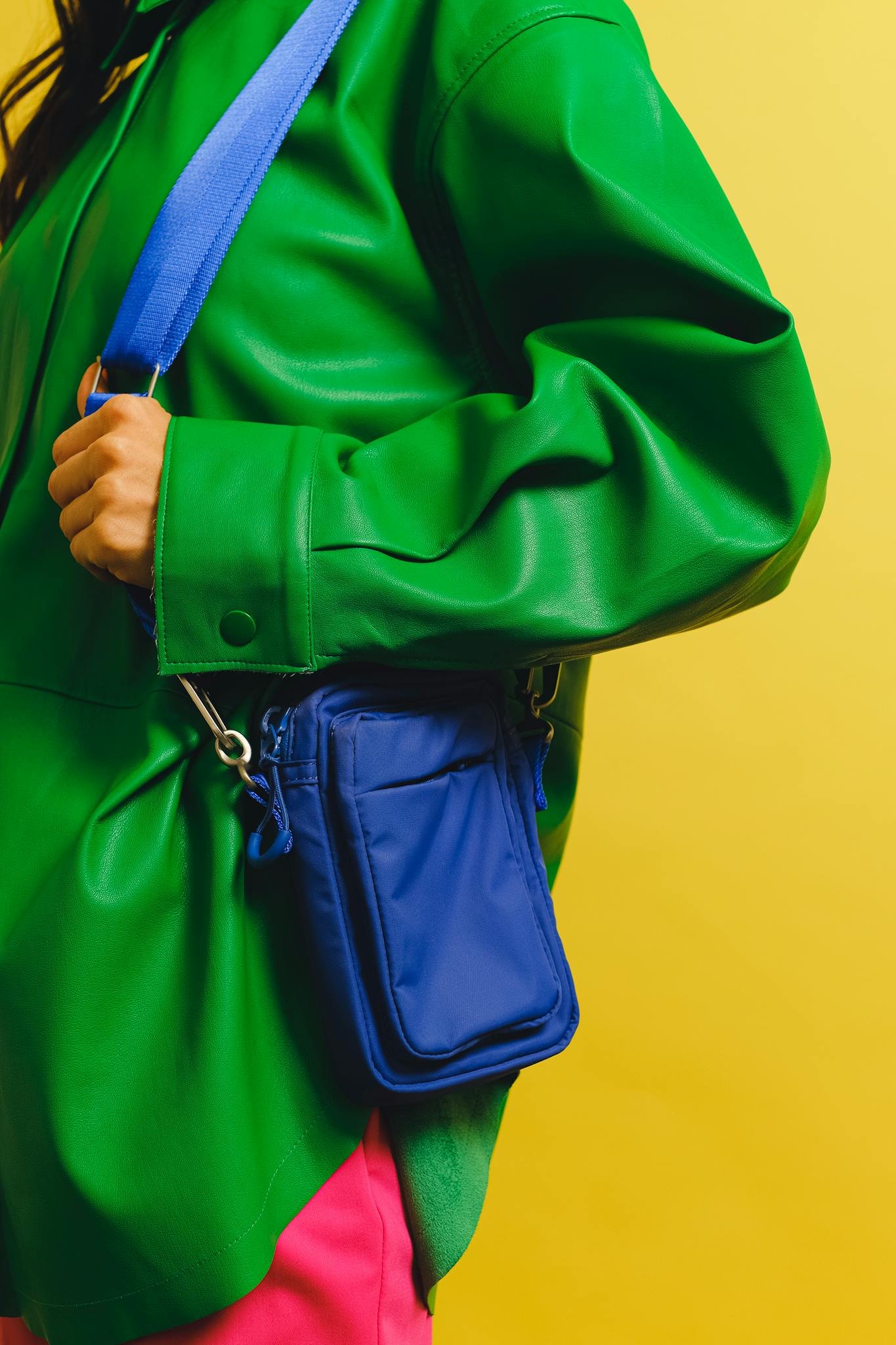 Stylish fashion close-up of a woman in a green jacket holding a blue bag against a yellow background.