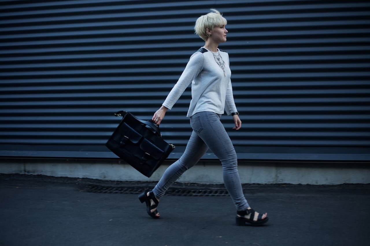 Home Stylish woman with blonde hair walking confidently along a city street carrying a leather bag.