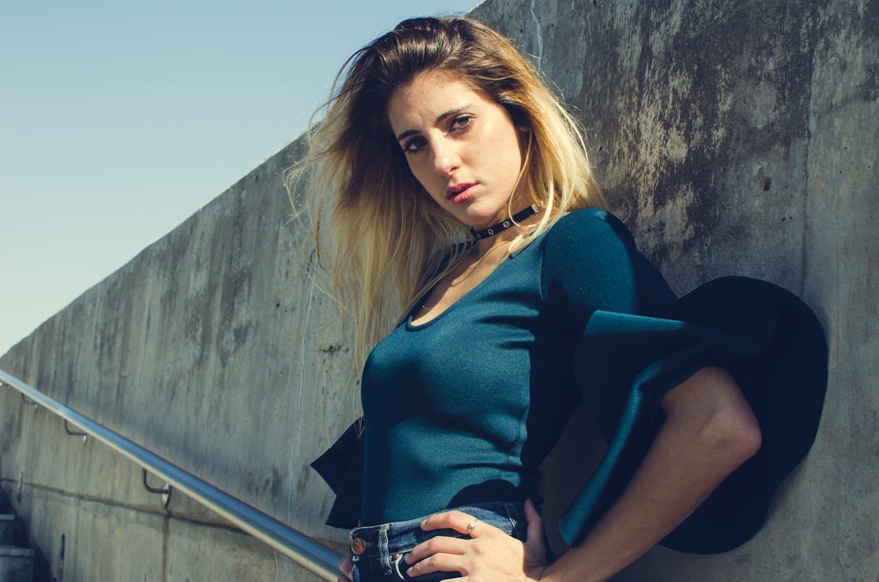 Home Fashionable woman with blonde hair posing outdoors against a concrete wall in urban setting.